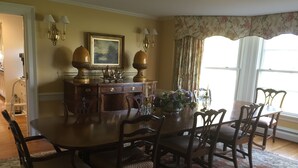 Un comedor con una gran mesa de madera, seis sillas, un valance de ventana con estampado floral y un cuadro en la pared.
