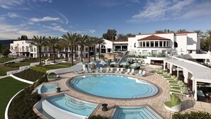 Un complexe hôtelier doté d’une grande piscine centrale, de plusieurs espaces de détente agrémentés de parasols, et d’un bâtiment blanc surmonté d’un toit rouge.