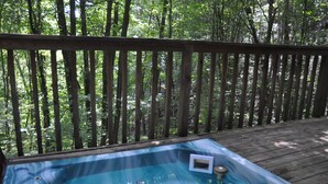 Een hottub op een houten terras, omringd door een bos.