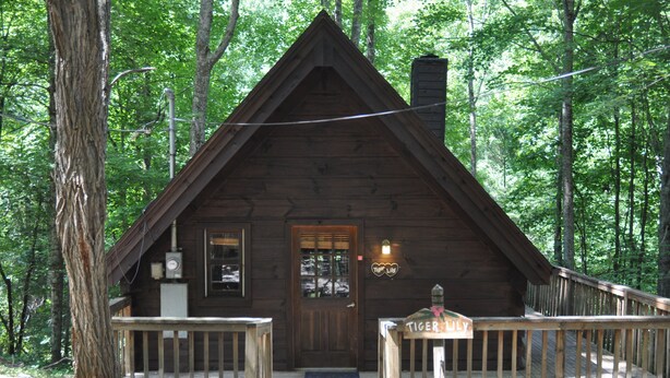 Een houten vakantiehuisje met een veranda, een schoorsteen en een bordje met de tekst 'Tiger Lily'.
