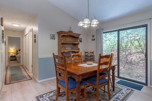 Un coin repas avec une table en bois, des chaises, un lustre et une vue à travers une porte vitrée.