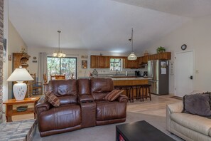 A living room with a brown leather sofa, a dining area with wooden chairs, a kitchen with wooden cabinets, and a refrigerator.