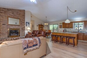 A spacious living area with a fireplace, a dining table, and a kitchen with wooden cabinets and a large island.