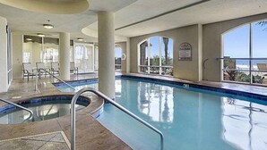 An indoor swimming pool with clear views of the ocean through large windows. - Agape Bay - Sienna on the Coast Unit 102 (Gulfport)