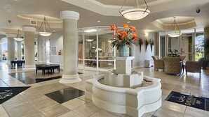 A spacious lobby with a central fountain, large columns, and modern lighting fixtures. - Agape Bay - Sienna on the Coast Unit 102 (Gulfport)