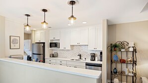 Una cocina moderna con gabinetes blancos, electrodomésticos de acero inoxidable e iluminación colgante.