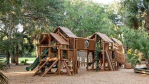 Una estructura de madera para juegos con toboganes y zonas de escalada, rodeada de árboles.