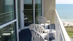 Ein Balkon mit Meerblick, ausgestattet mit zwei weißen Kunststoffstühlen und einer Glastür zu einem Innenraum.
