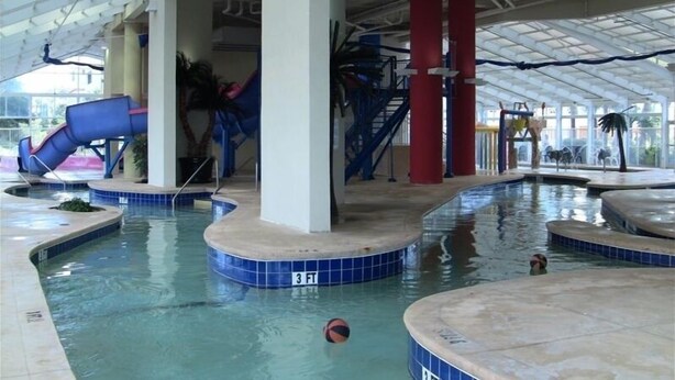 Ein Hallenbad mit blauer Rutsche, Whirlpool und Wasserspielbereich.