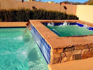 Ein Schwimmbecken mit Wasserfall und separatem Whirlpool-Bereich.