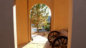 A stone pathway leading to a bench area with two wooden wheels, framed by a yellow wall. - Albuquerque Home w/ Heated Pool & Hot Tub Near Balloon Fiesta (Albuquerque)