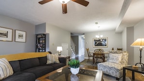 A living room with a dark sofa, a patterned armchair, a glass coffee table with a plant, and a wooden ceiling fan. - Downtown Townhouse Near Rupp Arena (Lexington)