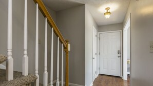 A hallway with a wooden staircase, carpeted steps, and a white door at the end. - Downtown Townhouse Near Rupp Arena (Lexington)