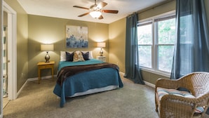 A bedroom with a bed, two bedside lamps, a ceiling fan, a wicker chair, and a window with curtains. - Downtown Townhouse Near Rupp Arena (Lexington)