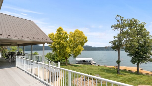 Une terrasse couverte avec des meubles d’extérieur, une pelouse avec des arbres et une vue sur un lac et des montagnes.