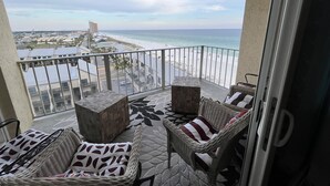 A balcony with wicker furniture and a view of the beach and ocean.