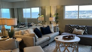 A modern living room with a sofa, armchairs, a coffee table, and a view of the city through large windows.