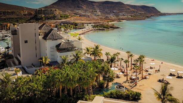 Un hotel frente al mar con piscina, playa y palmeras.