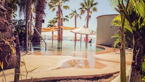 Zona de piscina con palmeras, sombrillas y un flotador salvavidas.