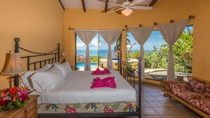 Une chambre d’hôtel avec un lit, un ventilateur de plafond, une vue sur l’océan et un balcon avec une chaise.