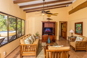 A spacious living room with a wooden sofa set, a television, and a ceiling fan.