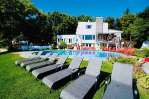 Un área de piscina con sillones de descanso, una piscina y un edificio con chimenea de piedra.