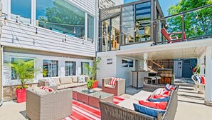 Un amplio espacio al aire libre con mobiliario de mimbre, un tapete rojo y blanco a rayas, y vista al interior del edificio.