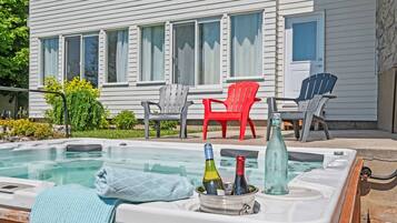 A hot tub with bottles and a towel, surrounded by outdoor chairs and a house in the background.
