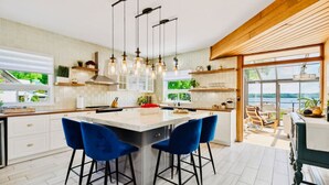 Cocina moderna con una isla central, taburetes de bar, iluminación colgante y ventanas amplias con vistas al exterior.