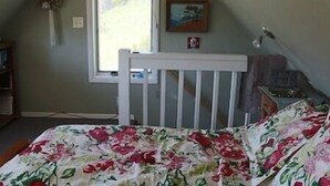 Una habitación con una cuna blanca, una ventana con vistas y un cuadro en la pared.