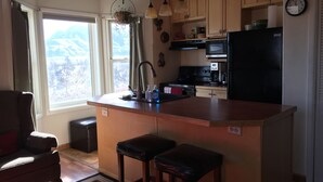 Cocina con armarios de madera, refrigerador negro, microondas y cafetera. Se ve una ventana con vistas a las montañas.