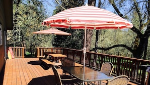 A wooden deck with a table and chairs, two striped umbrellas, and a railing.