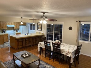 A kitchen with wooden cabinets, a central island, and a dining area with a table set for four. - Peaceful Rogue Riverfront Home on 3 Acres! (Grants Pass)