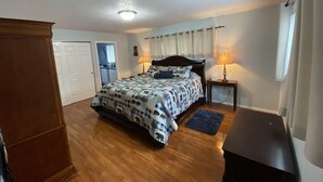 A bedroom with a bed, a nightstand, a lamp, a dresser, and a window with curtains.
