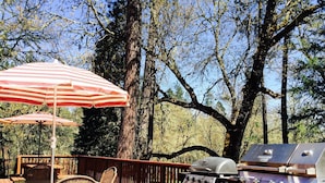 A deck with a grill, wicker chairs, and striped umbrellas.