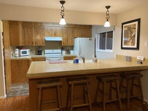 A kitchen with wooden cabinets, a white refrigerator, a microwave, a stove, and a large island with stools.