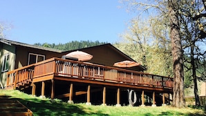 A wooden deck with outdoor umbrellas, a staircase leading to a covered area, and a tree in the background.
