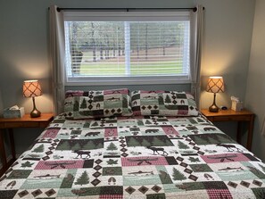 A bed with a quilt featuring wildlife patterns, flanked by bedside tables with lamps, and a window with blinds.
