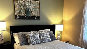 A neatly made bed with a quilted bedspread, two matching pillows, a decorative wall piece above the bed, and two bedside lamps. - Downtown OS.  Quite & Walkable.  2 Sm Pets. Refurbished.  GolfCart
Rental  (Ocean Springs)