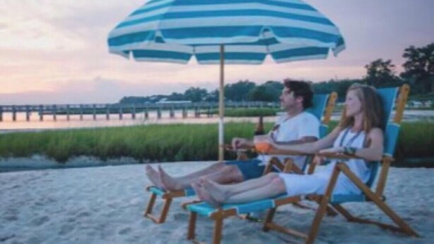 Two people sitting on beach chairs under a striped umbrella on a sandy beach with a body of water in the background. - Downtown OS.  Quite & Walkable.  2 Sm Pets. Refurbished.  GolfCart
Rental  (Ocean Springs)