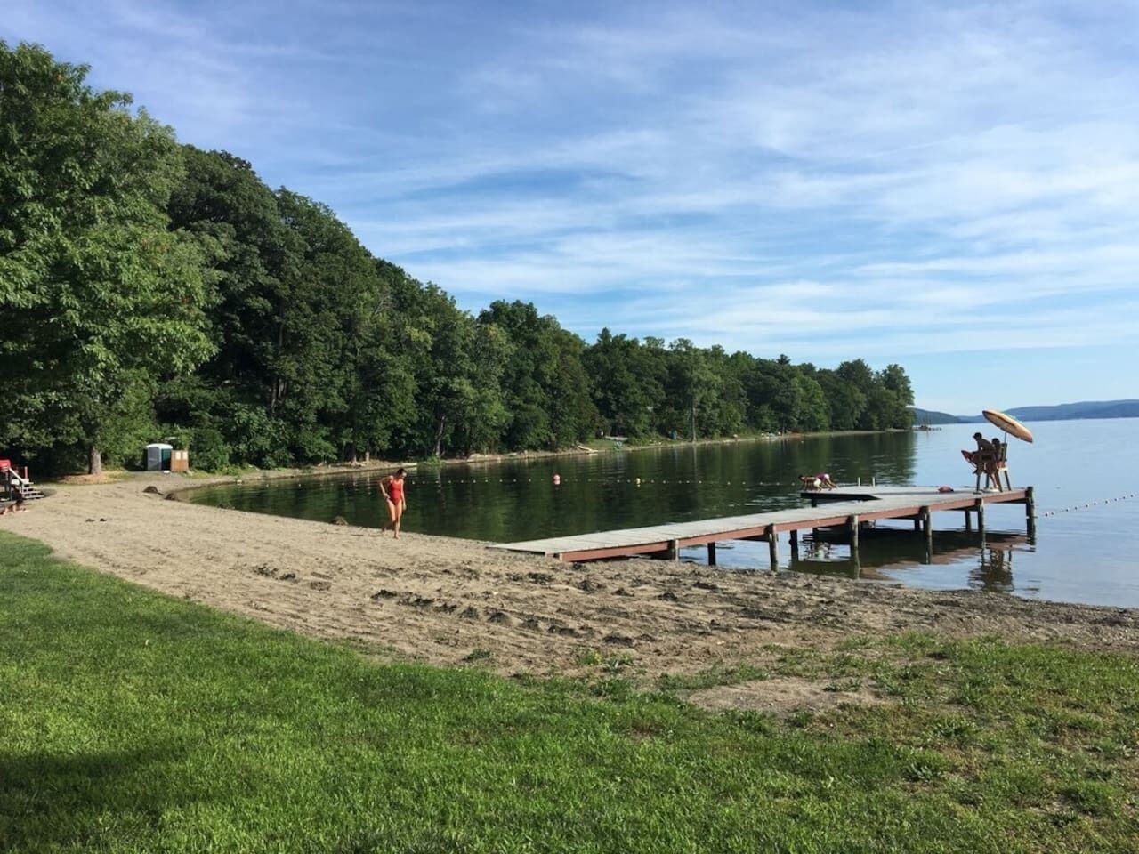 Une plage au bord d’un lac, avec une jetée en bois qui s’avance dans l’eau, le tout entouré d’une végétation luxuriante.