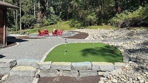 Een klein buitengebied met een putting green, rode stoelen en een houten constructie.