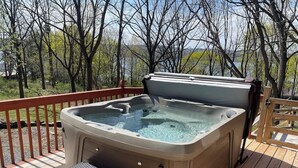 Een hottub op een houten terras met uitzicht op bomen en een waterpartij.