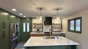 Een keuken met een centraal eiland, roestvrijstalen apparatuur en hanglampen.