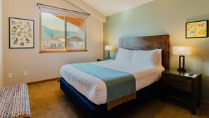 A hotel room with a large bed, two bedside tables with lamps, a window with a view of buildings, and two wall-mounted artworks.