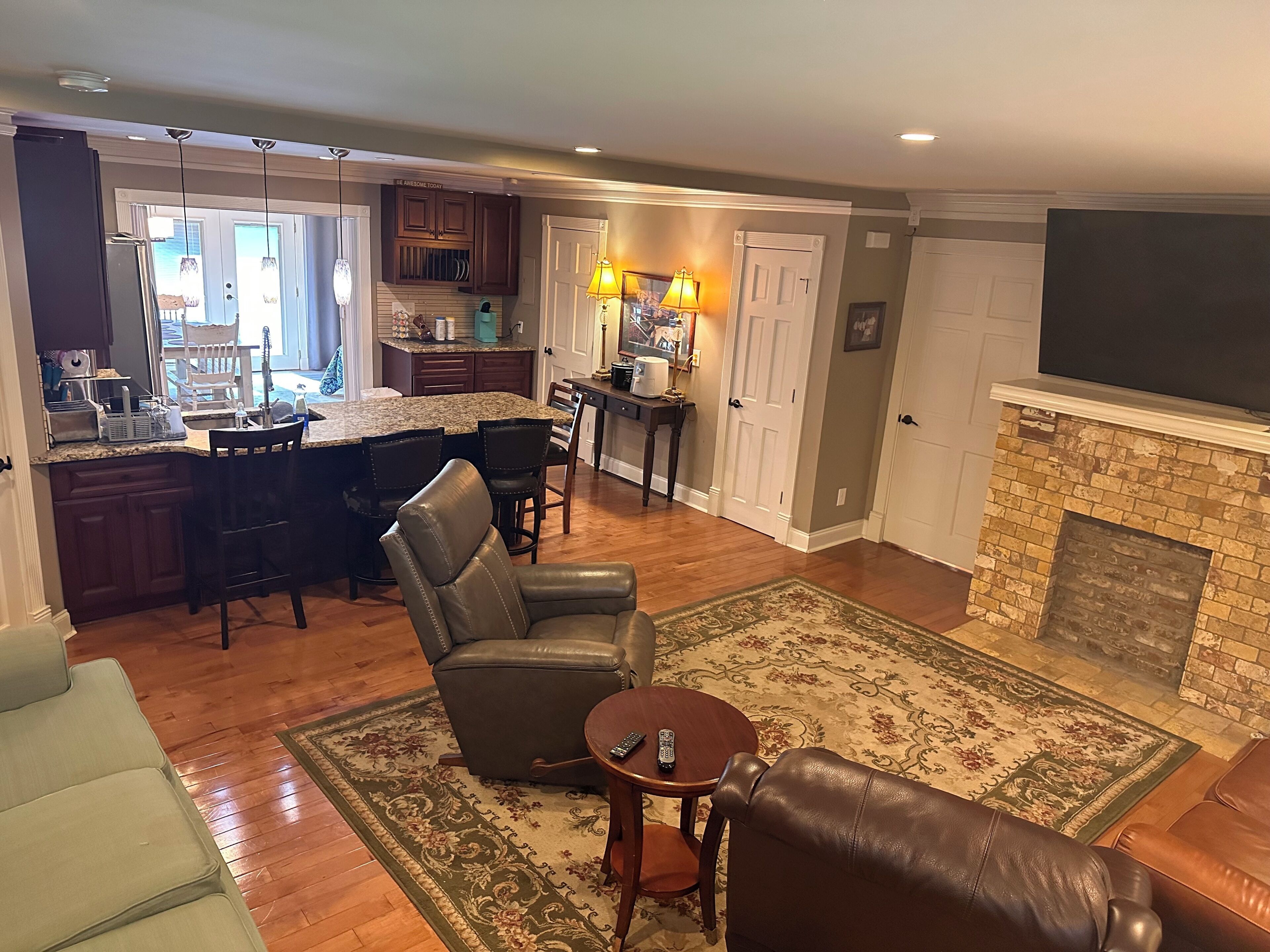 A spacious living room with a fireplace, a dining area with a kitchen in the background, and a view of the outdoors.