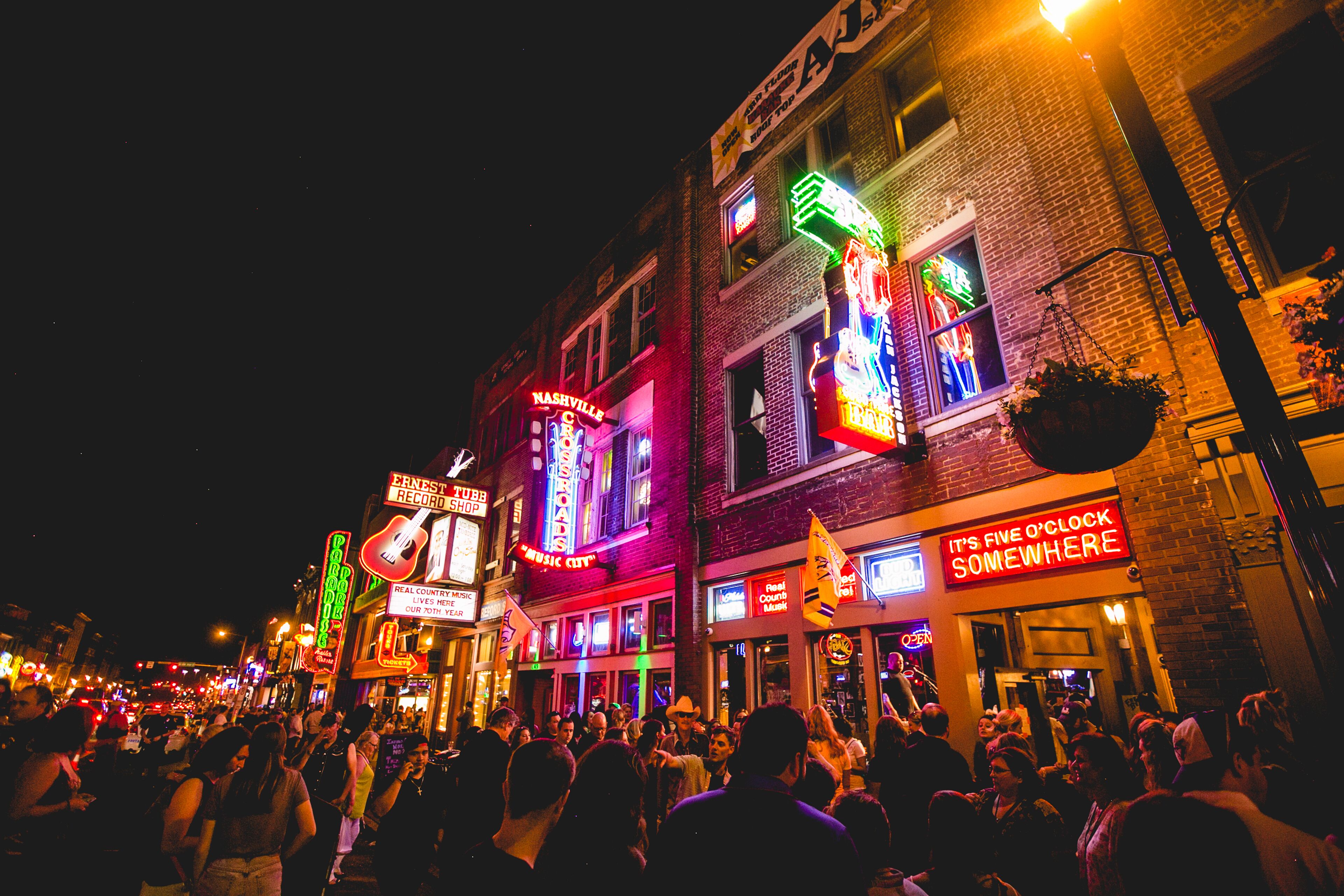 A crowded street at night with illuminated storefronts and a crowd of people.