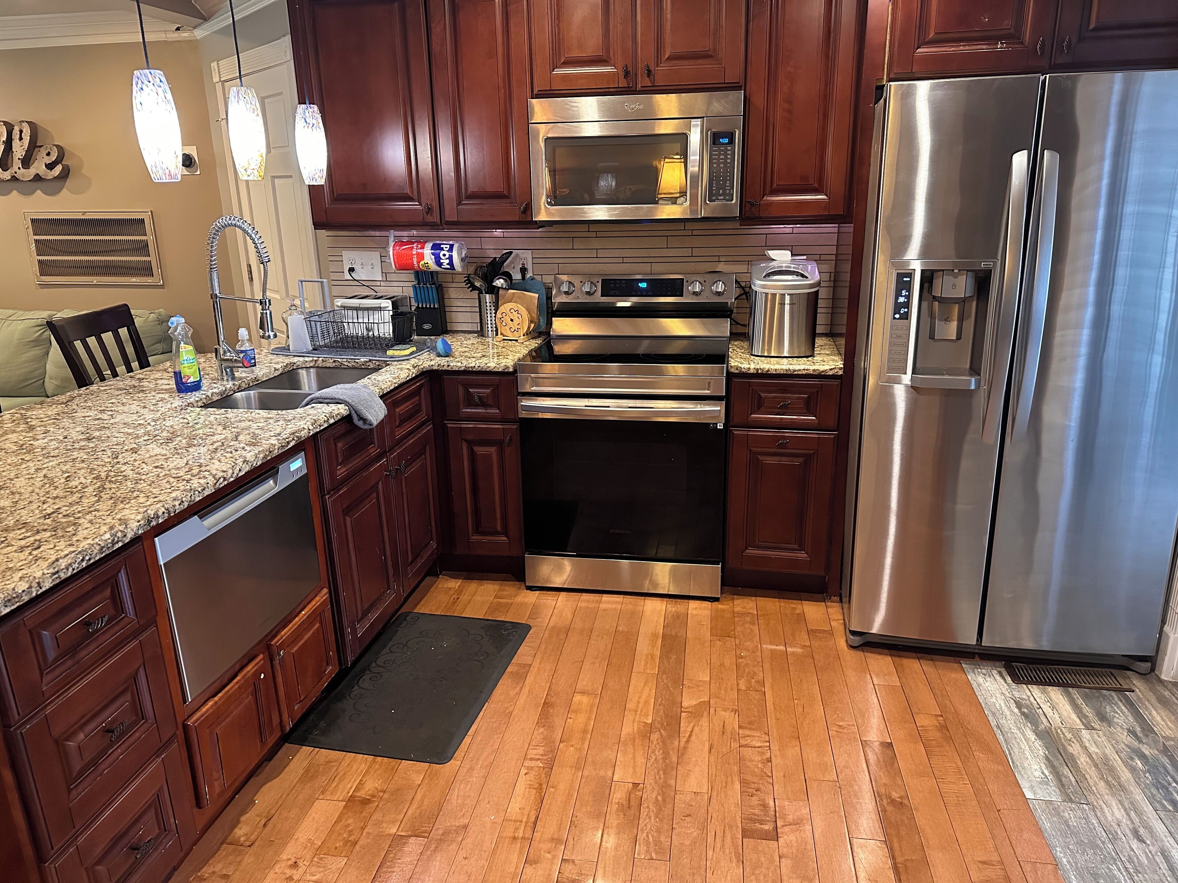 A modern kitchen with wooden cabinets, stainless steel appliances, granite countertops, and a black doormat.