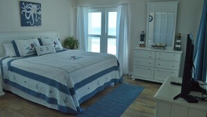 Un dormitorio con cama, cómoda, televisor y ventana con cortinas.