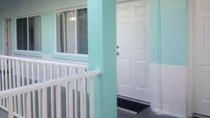 A building exterior with teal and white walls, a white door, and a small balcony with a white railing.